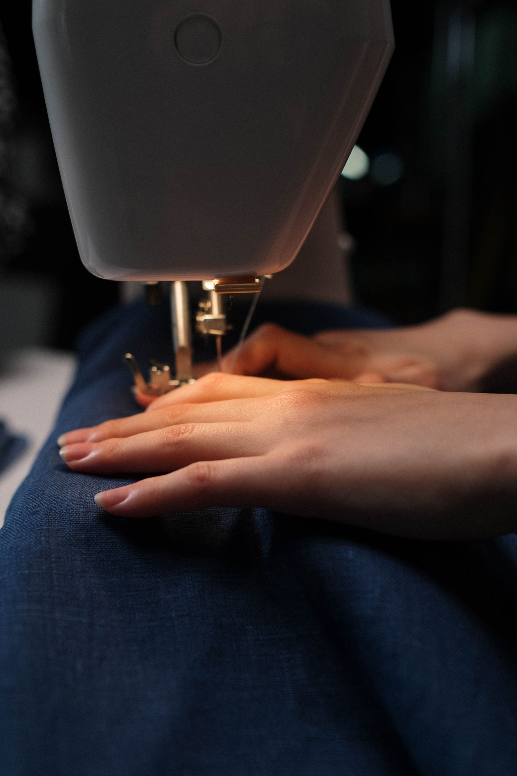 Hands guiding blue fabric through a sewing machine